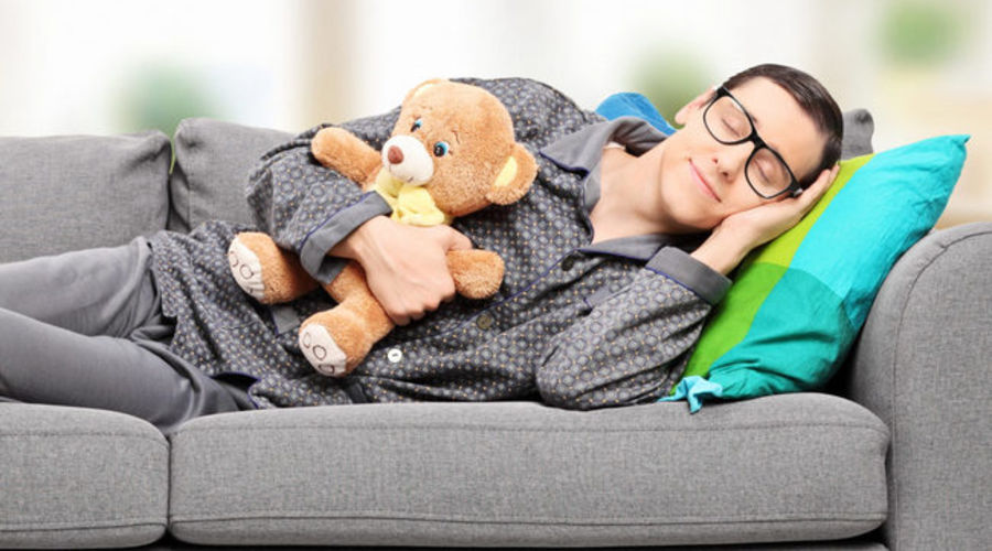 Young man in pajamas sleeping on sofa at home with teddy bear 